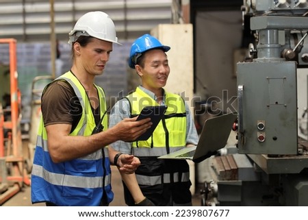 Technician engineer in protective uniform with hardhat standing and teaching apprentices or colleague worker to use computerized machine control at heavy industry manufacturing factory