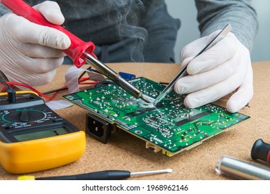 Technician engineer in workshop. He takes tin with a soldering iron and puts it on microcircuit.  Repairman in gloves is soldering circuit board of electronic device. - Powered by Shutterstock