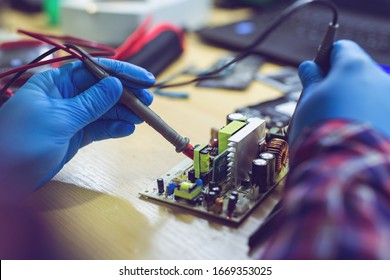 Technician engineer in workshop. Repairman is checking circuit board of electronic device.