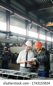 Technician In Formalwear Using Tablet While Engineering Industrial Machine With Factory Worker In Workshop