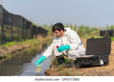 A Technician In Full Body Protective Suit Collecting Sample Of Water .Portable Water Quality Measurement .Water Quality For Agriculture. Checking Water Ph On Field