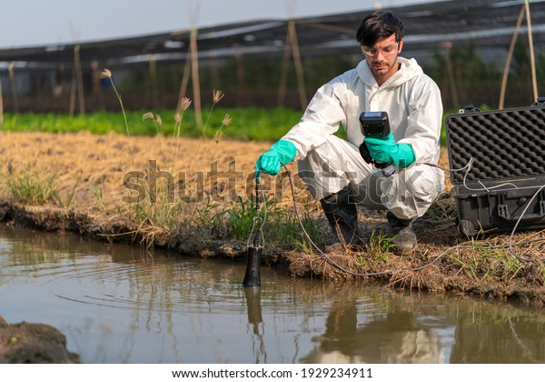 A technician in full body\
protective suit collecting sample of water ,Portable water quality\
measurement ,water quality for agriculture ,ph checking on\
field