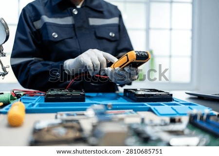 Technician in gloves tests computer hard drives with a handheld meter at an electronics repair bench, showing data recovery, maintenance, and hardware diagnostics in a clean workspace