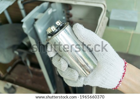 Technician hand with air conditioner capacitor, Checking air compressor capacitor, Home appliances repair service.