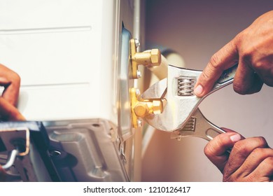 Technician hand using fix wrench to tighten outdoor unit of air condition, Man holds a wrench in his hand. - Shutterstock ID 1210126417