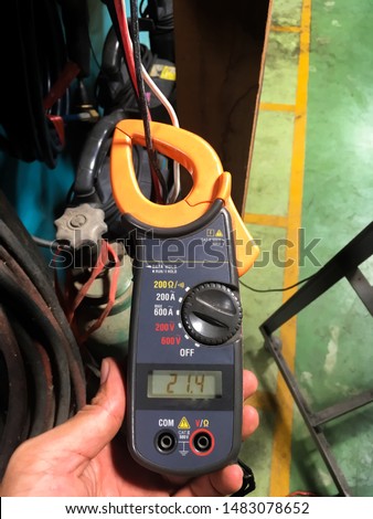 Technician hands use digital clamp meters for measure the amperage of electrical appliances in the maintenance department of the factory.