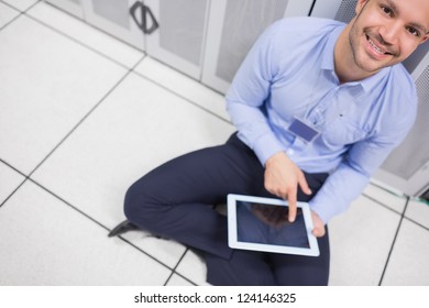 Technician happily using tablet pc in data center sitting on floor
