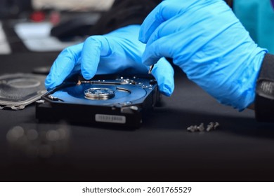 A technician in a hard disk assembly lab is disassembling and repairing a hard disk on a workbench, wearing gloves and holding a screwdriver to repair the hard disk or recover data.