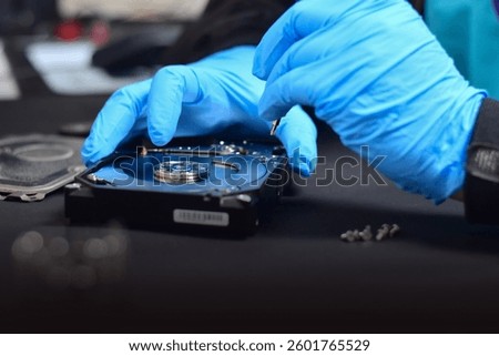 A technician in a hard disk assembly lab is disassembling and repairing a hard disk on a workbench, wearing gloves and holding a screwdriver to repair the hard disk or recover data.