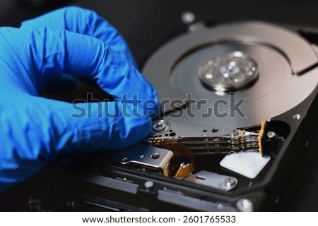 A technician in a hard disk assembly lab is disassembling and repairing a hard disk on a workbench, wearing gloves and holding a screwdriver to repair the hard disk or recover data.
