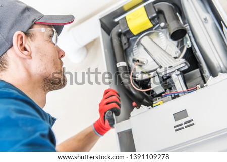 Technician and the Heater Issue. Caucasian Worker Looking Inside Central Gas Heater Trying to Fix the Problem.