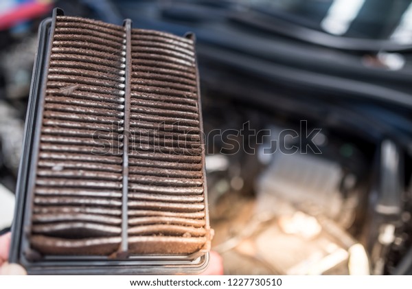 Technician\
holding dirty air filter for car. , clogged air filter over a car\
engine during general auto\
maintenance.