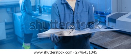 Technician holding open binder with documents in laboratory setting.
