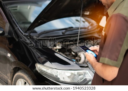 Technician holding smartphone to watch the oil function monitor. Mobile device screen show fuel oil status. Concept of using digital technology devices for car fix. Selective focus. Blur background