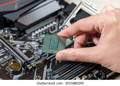 A technician holds the CPU Intel against the background of the motherboard Gigabyte. Computer parts. PC assembly concept