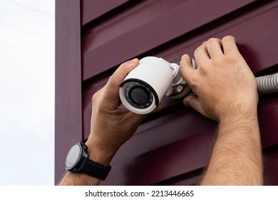 Technician installing CCTV camera on wall outdoors, closeup. A video surveillance camera in the hands of a technician. Installation of outdoor video surveillance in close-up.