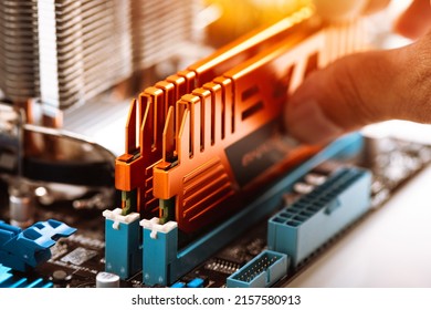 Technician installing DDR3 memory module with orange heatsink to the mainboard. Upgrading PC computer concept.