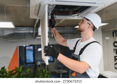 Technician installing a new filter and checking the ceiling mounted air conditioning unit with a screwdriver