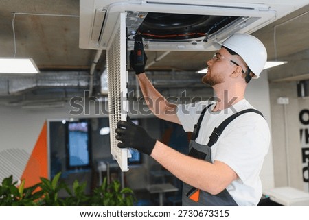 Technician installing a new filter and checking the ceiling mounted air conditioning unit with a screwdriver