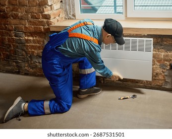 Technician installing white electric convector heater on brick wall indoors. Concept of energy efficiency, utility services, and winter comfort for residential heating materials and media use.