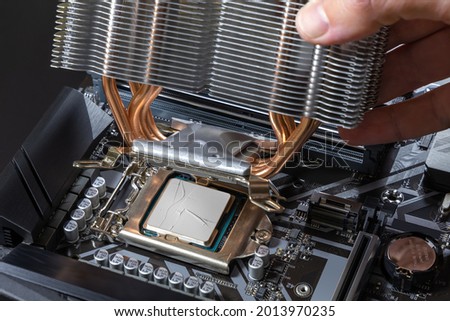 A technician installs an aluminum air-cooled heatsink on a desktop CPU covered with heatsink paste. Air Cooler CPU. PC assembly and modernization