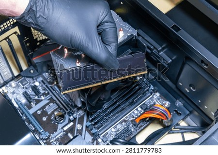 Technician installs a black DDR memory module into a DIMM slot on a motherboard. Assembly or upgrade of a modern PC. Expensive PC components