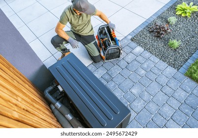 A technician kneels beside an outdoor HVAC unit, carefully organizing tools from a portable toolbox. The setting features a modern residential patio with stone pavers and greenery - Powered by Shutterstock