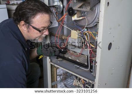 Technician  looking over a gas furnace with a flashlight before cleaning it. 