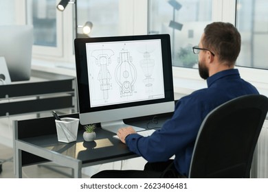 Technician making digital engineering drawing on computer at desk in office, back view