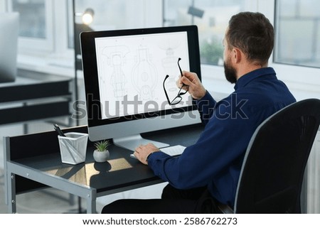 Technician making digital engineering drawing on computer at desk in office, back view