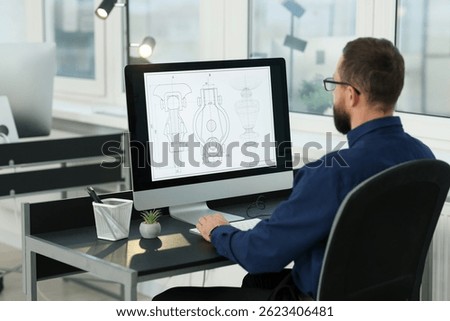 Technician making digital engineering drawing on computer at desk in office, back view