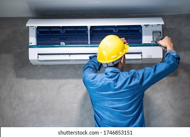 Technician Man Repairing ,cleaning And Maintenance Air Conditioner On The Wall With Screw Driver In Bedroom Or Office Room.On Site Home Service,Business ,Industrial Concept.