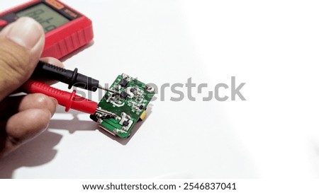 A technician is measuring the PCB board of an electronic device using a red digital multitester with the display saying 