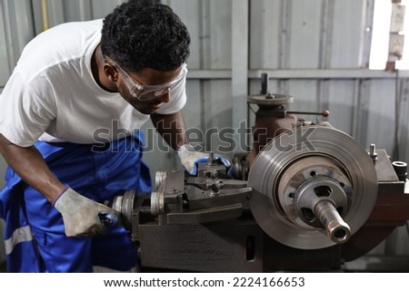 Technician mechanic or worker man in protective uniform using metal lathe machine operate polishing car disc brake at garage. Maintenance automotive and inspecting vehicle part concept