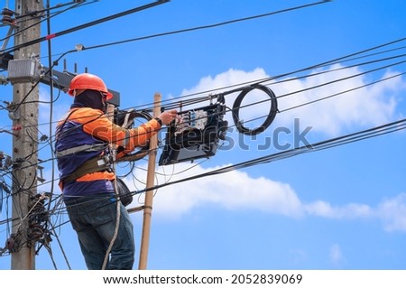 Technician on ladder is Installing Fiber Optic Telephone system in Internet Splitter box on Electric power Pole against blue sky