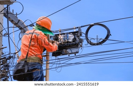 Technician on ladder is Repairing Fiber Optic Cable in Internet Splitter Box on Electric Pole against blue sky background