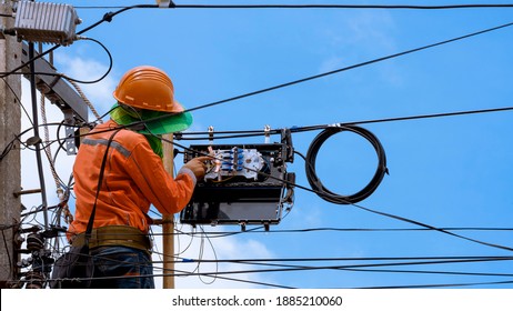 Technician on wooden ladder Checking Fiber Optic Cables in Internet Splitter Box on Electric Pole against blue sky background - Shutterstock ID 1885210060