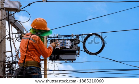 Technician on wooden ladder Checking Fiber Optic Cables in Internet Splitter Box on Electric Pole against blue sky background