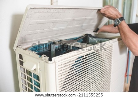 A technician opens up the top hatch of the outdoor compressor unit of a Split type air conditioner. Repair or maintenance work.