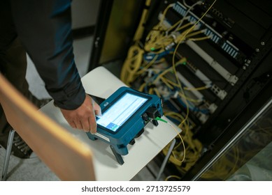 A technician operates a network analyzer in a server room, surrounded by cables and hardware, ensuring optimal connectivity and performance for the system.