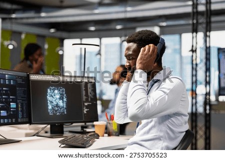 Technician optimizing performance using AI LLM chatbot, enjoying songs. African american IT expert putting on audio headset, using artificial intelligence assistant to automatize workflows