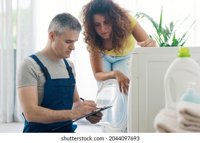 Technician performing a check-up on a washing machine, he is writing on a clipboard, repair service concept