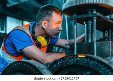 Technician performs hands-on maintenance and precise machine adjustment on heavy industrial equipment in a traditional metal workshop, showing manual skill, inspection, and craftsmanship.