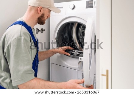 Technician performs maintenance on an automatic washing machine, inspecting rubber and drum with internal components in a laundry room, focused on ensuring optimal performance and reliability.
