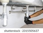 Technician plumber using a wrench to repair a water pipe under the sink. Concept of maintenance, fix water plumbing leaks, replace the kitchen sink drain, cleaning clogged pipes is dirty or rusty.