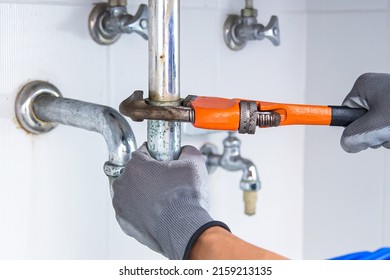 Technician plumber using a wrench to repair a water pipe under the sink. Concept of maintenance, fix water plumbing leaks, replace the kitchen sink drain, cleaning clogged pipes is dirty or rusty. - Shutterstock ID 2159213135