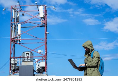 Technician programmer connects remotely to transfer data. Male telecommunications engineer works near a communication tower to check maintain 4G and 5G internet networks and cellular communications.