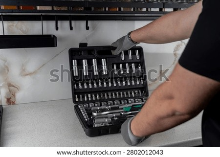 Technician in protective gloves opening a large plastic toolkit case containing a professional socket wrench and bit set on a kitchen countertop.