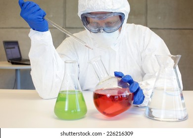 Technician In Protective Uniform,goggles,mask,gloves Working In Lab With Pipette And Glassware 