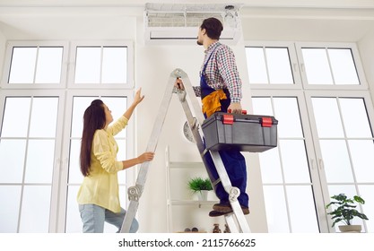 Technician repairing AC on his typical working day. Man climbs ladder with toolbox in order to check, do disinfection or fix troubles in modern white wall mounted air conditioner in young lady's home Foto Stock